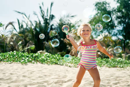 Little happy girl playing soap bubbles on the topical beachの写真素材