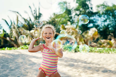 Little happy girl playing soap bubbles on the topical beachの写真素材