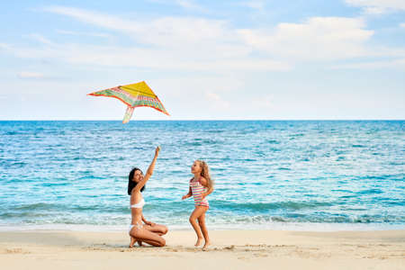 Mother and daughter having fun flying a kite on tropical beachの写真素材