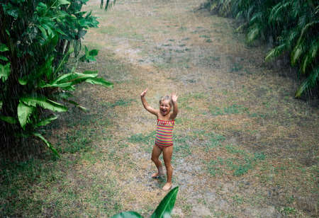 Pretty little girl enjoy the rain and dancing on the street in summerの写真素材