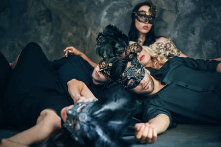 Group of friends in masquerade carnival mask sitting on floor relax after partyの写真素材