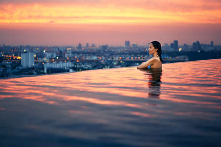 Young woman relax in swimming pool on roof top during amazing sunset and enjoy cityscapeの写真素材