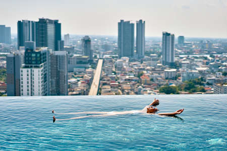 Young woman relaxing in roof top swimming pool and floating in waterの写真素材