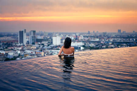 Young woman relax in swimming pool on roof top during amazing sunset and enjoy city viewの写真素材