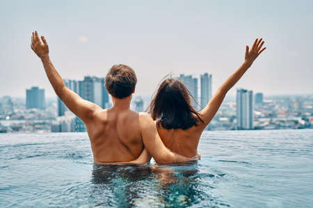 Young happy couple in love with arms up having fun in swimming pool