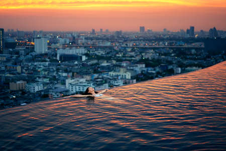 Young woman relax in swimming pool on roof top during amazing sunset