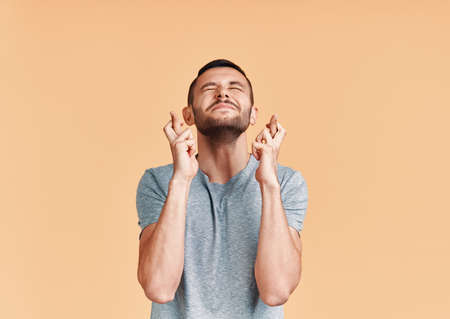 Young man making a wish and ask for good luck with crossed fingers isolated on yellow backgroundの写真素材