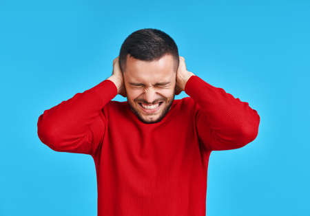 Handsome man covering his ears with hands afraid to hear bad news