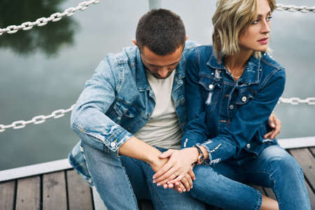 Beautiful fashionable couple posing on river bridge wearing denim jeansの写真素材