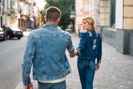 Beautiful young woman walking on the street and holding man by handの写真素材