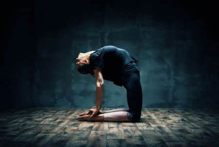 Young woman practicing yoga doing Camel pose in dark roomの写真素材