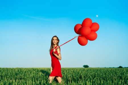 Freedom happy woman running with red balloons on green summer fieldの写真素材