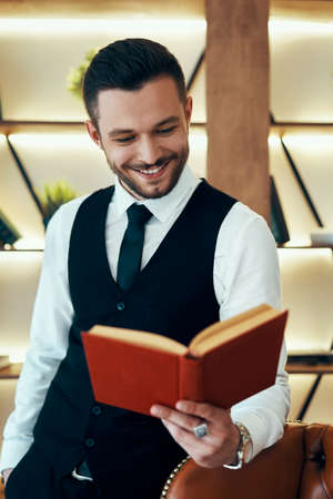Handsome young man in elegant suit reading a book in modern luxury interiorの写真素材