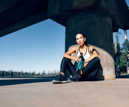 Young fitness woman relax after work out exercising in industrial city background near river. Sport...