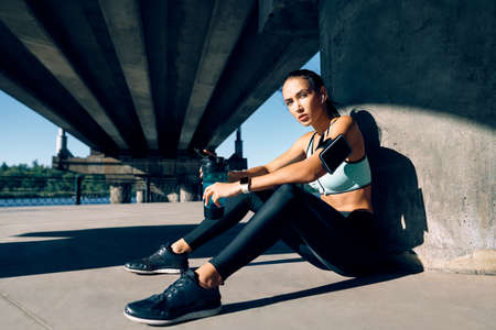 Young fitness woman relax after work out exercising in industrial city background near river. Sport conceptの写真素材