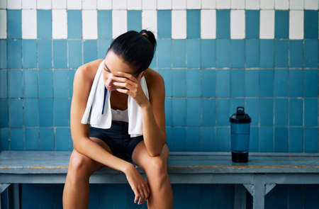 Tired fit woman with a towel in the locker room after hard workout. Stress, sport, failure concept                      の写真素材