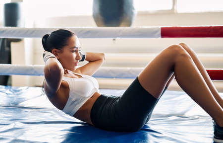Fit woman doing sit up exercise on mat at boxing studio. Abs workout training for abdominal muscles.