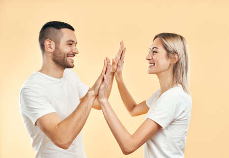 Portrait of young smiling couple giving high five to each other over studio background. Man and woman playing patty cakeの写真素材
