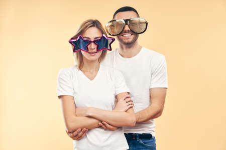 Young happy couple in funny party glasses on beige background. Fun conceptの写真素材