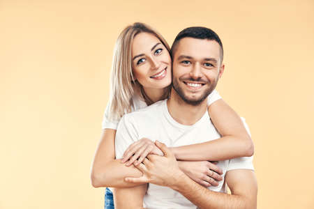 Happy smiling couple in love on beige background. Man carrying his girlfriend piggyback. Love,...