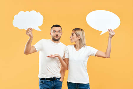 Emotional woman and man holding paper thought bubbles over yellow background. relationship conceptの写真素材