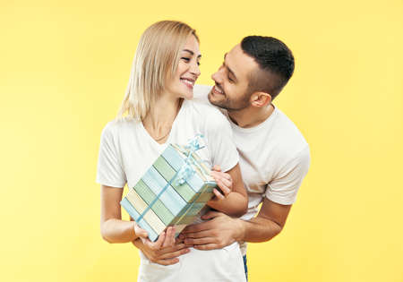 Young happy couple with gift box over yellow background. Present, holiday, celebration concept