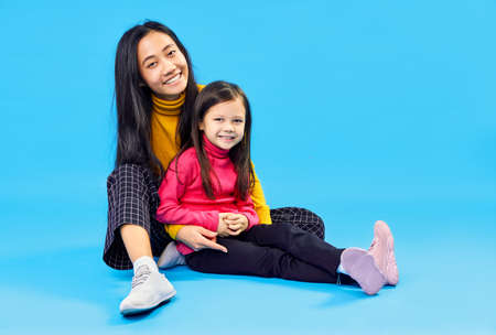 Happy smiling mother hugs her little cute daughter posing on blue studio background