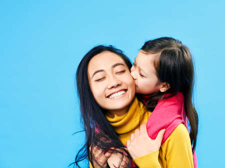 Little cute daughter hug and kissing her happy mother isolated on blue background. Family love conceptの写真素材
