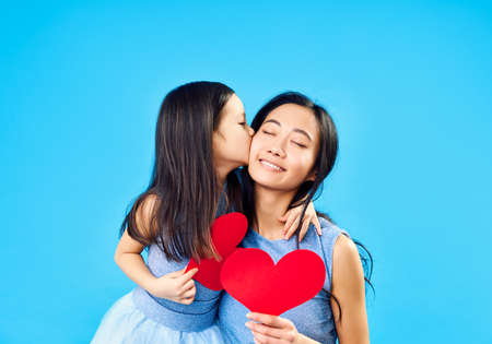 Little girl kissing her mom holding paper heart on blue backgroundの写真素材
