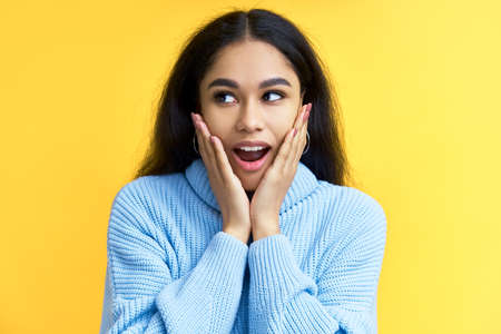 Young happy and surprised black woman holds cheeks by hands isolated on yellow backroundの写真素材