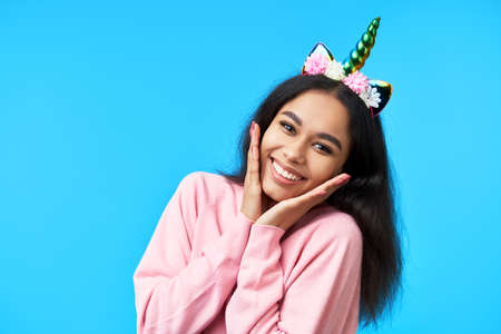 Happy smiling woman with unicorn horn posing over blue background.