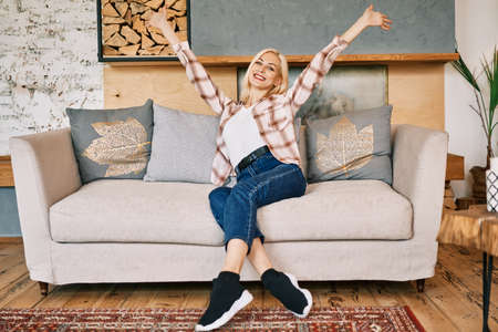 Happy smiling woman with raised hands sitting on sofa at homeの写真素材