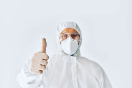 Doctor in protective medical suit showing thumbs up. Focus on handの写真素材