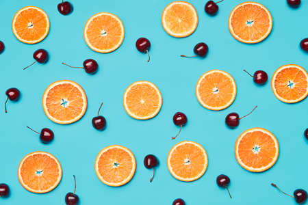 Orange slices and sweet cherries on blue backgroundの写真素材