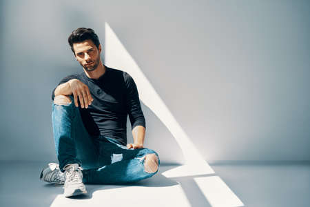 Young handsome man portrait sitting on floor in sun lights with copy spaceの写真素材