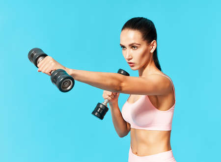 Young sporty woman in sportswear doing exercise with dumbbells on blue backgroundの写真素材