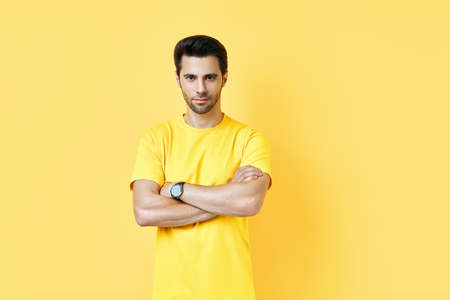 Happy smiling handsome man with crossed arms looking to camera over yellow background