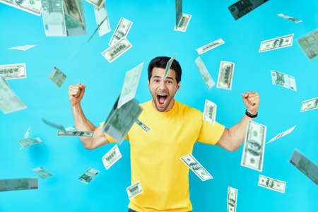 Happy excited man standing under money rain banknotes falling downの写真素材