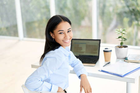 Smiling young African American businesswoman posing at her desk in a bright modern officeの写真素材