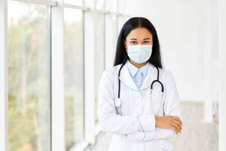 Female doctor wearing medical mask with arms crossed in hospital backgroundの写真素材