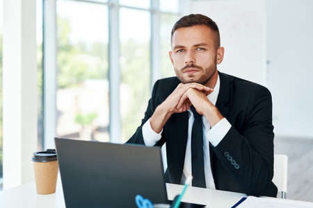 Confident young businessman in elegant suit posing in a bright modern office. sitting at his desk