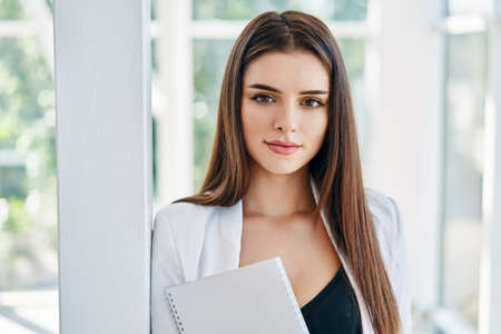 Confident business woman holding documents and looking at camera in modern creative officeの写真素材