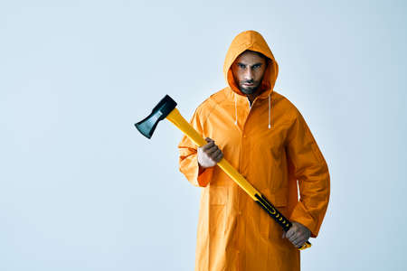 Young serious man in bright raincoat holding big axe in hands with copy space