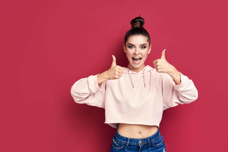 Happy smiling hipster woman showing thumbs up on pink background