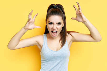 Screaming emotional angry young woman close up portrait over yellow background