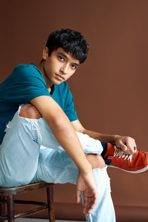 Stylish handsome mixed race man posing on studio sitting on a chair looking to camera
