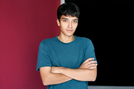 Young trendy handsome man with crossed arms posing on studio backgroundの写真素材