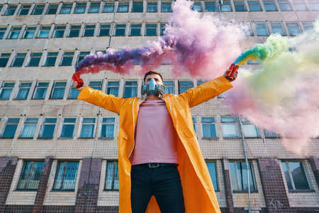Young man in respirator mask hold smoke bombs in raised handsの写真素材