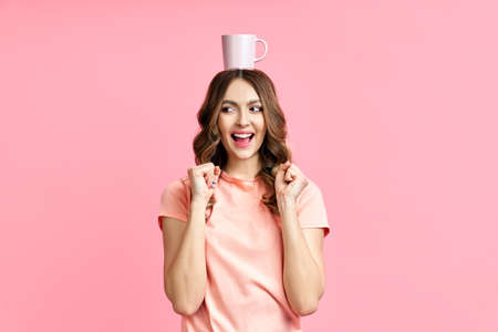Smiling pretty woman having fun with cup of coffe on her head on pink backgroundの写真素材