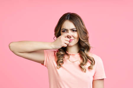 Smells bad, woman pinching nose with disgust on pink backgroundの写真素材